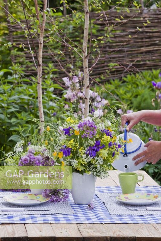 Set de table avec vase de bouquet de fleurs printanières contenant de l'allium, de l'iris, des vivaces de fleurs sauvages et des graminées.