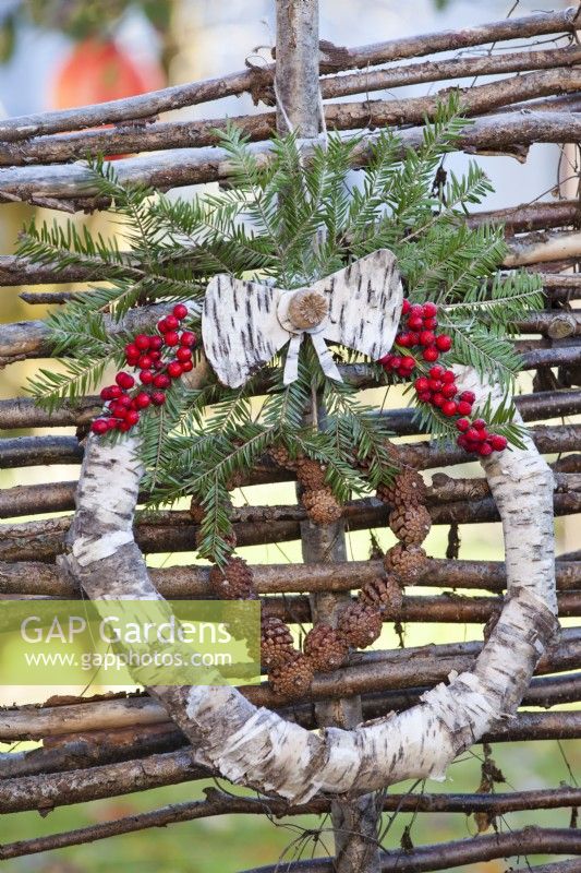 Couronne d'hiver faite d'écorce de bouleau, de branches d'épinette, de cônes et de baies rouges accrochées à une clôture.