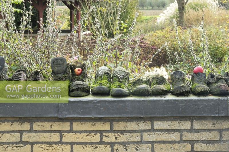 Vieilles chaussures de travail couvertes de mousse dans une rangée comme décoration sur le mur du jardin.