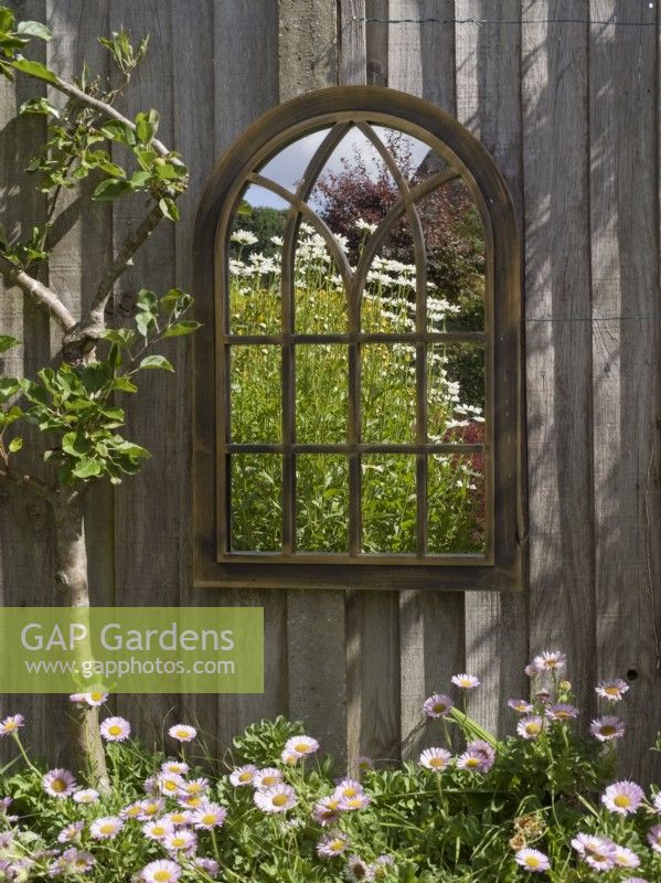 Réflexions de jardin dans un miroir gothique suspendu à une clôture de jardin