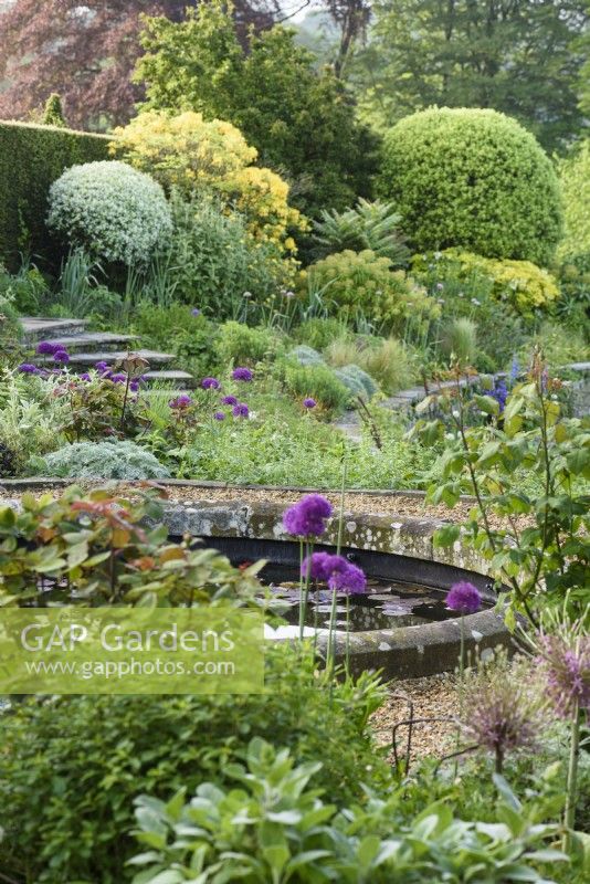 Jardin à la française avec bassin circulaire et arbustes persistants taillés en mai