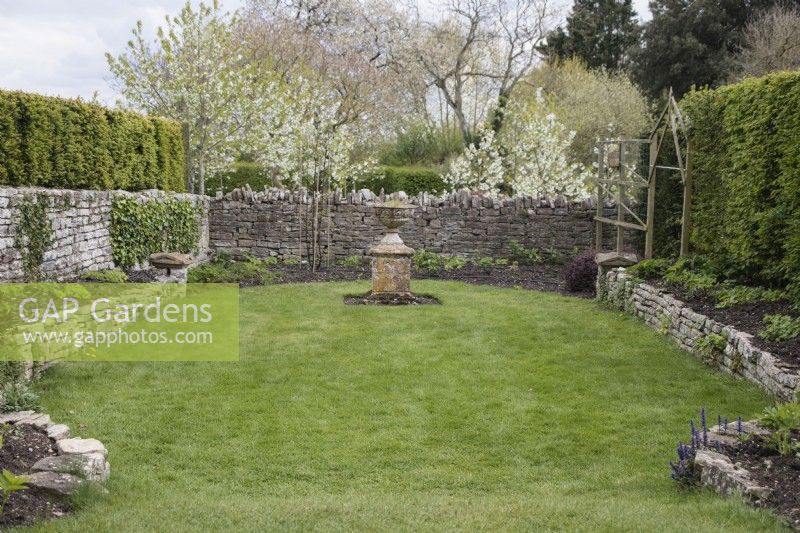 Petite zone de jardin contenue par des murs en pierre avec urne sur socle