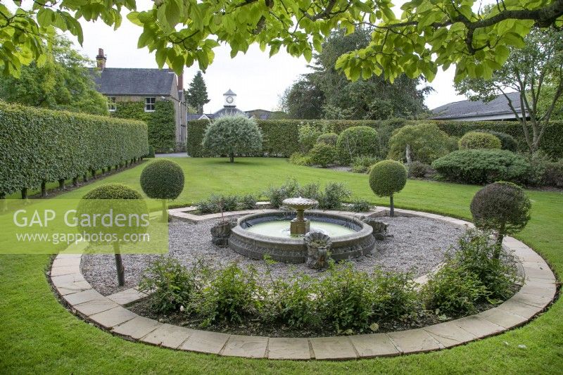 Parterre circulaire de gravier avec étang et fontaine et bordée de topiaires sucette au Burrows Gardens, Derbyshire, en août