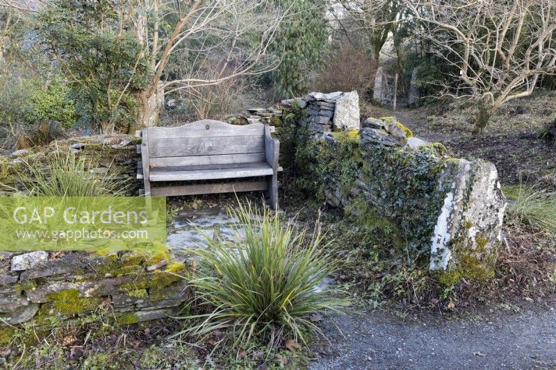 Un banc en bois niché dans l'angle d'un mur en pierres sèches. La maison du jardin, Yelverton, Devon