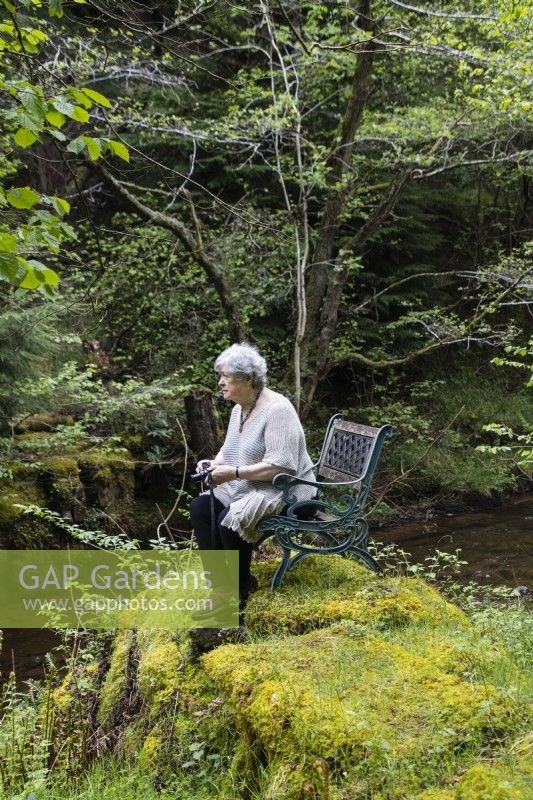 Visiteur assis sur une chaise sur un monticule couvert de mousse par stream holding camera. Peut.