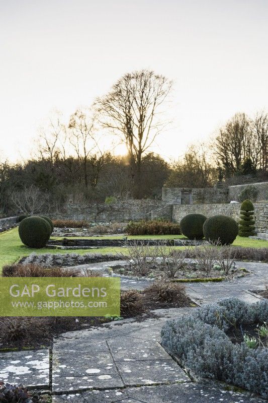 La terrasse Jewson à Cotswold Farm Gardens en février avec des parterres de fleurs géométriques et des ifs taillés.