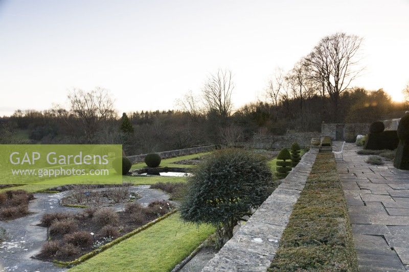 La terrasse Jewson à Cotswold Farm Gardens en février avec des parterres de fleurs géométriques et des conifères taillés, y compris des ifs et des buis.