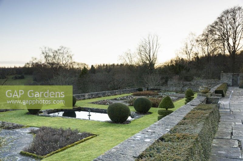 La terrasse Jewson à Cotswold Farm Gardens en février avec des parterres de fleurs géométriques et des conifères taillés, y compris des ifs et des buis.