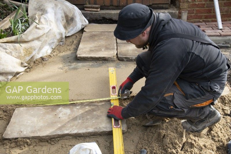 Un ouvrier mesurant une dalle de York Stone utilisée pour construire une terrasse.