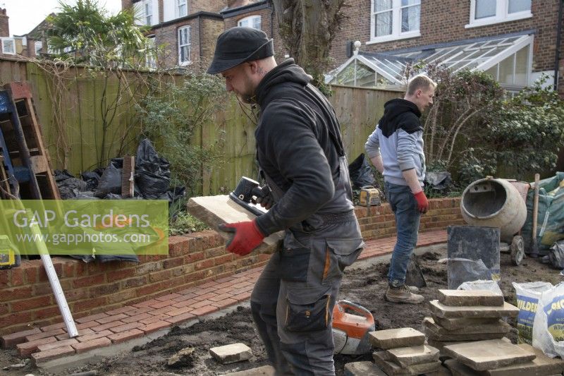 Un ouvrier portant une dalle de York Stone utilisée pour construire une terrasse lors de la rénovation d'un jardin londonien.