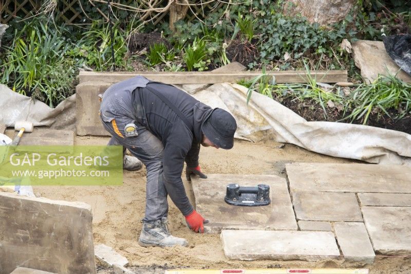 Un ouvrier pose des dalles de York Stone pour une terrasse lors de la rénovation d'un petit jardin londonien.