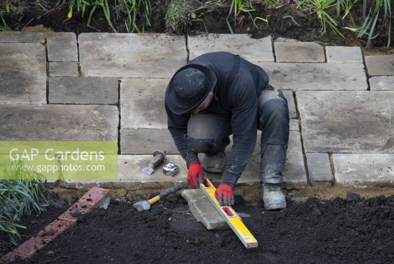 Un ouvrier préparant une dalle de York Stone à utiliser sur une terrasse lors de la rénovation d'un petit jardin londonien.