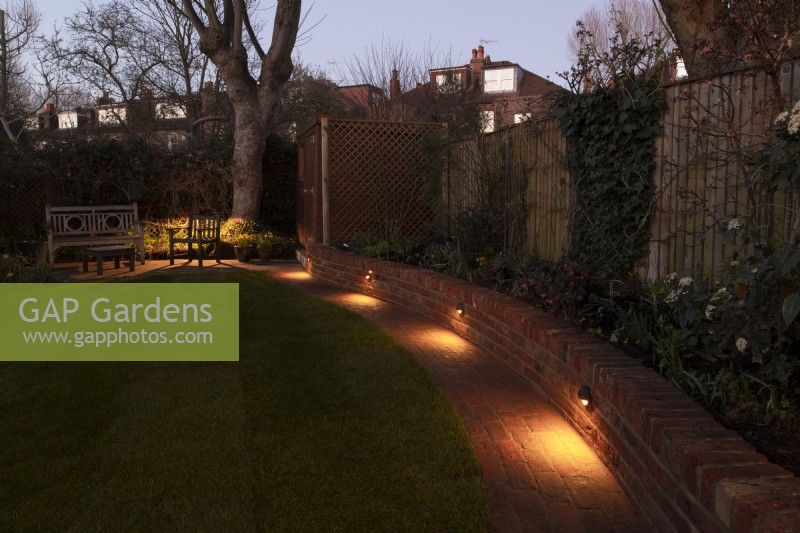 Un jardin de Londres après une cure de jouvence avec un nouveau muret de briques avec des spots le long d'un chemin de brique entouré de pelouse.