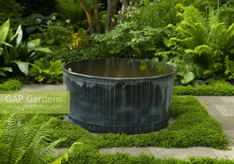 Une fontaine circulaire en métal entourée de fougères dans le Myeloma UK - A Life Worth Living Garden conçu par Chris Beardshaw au RHS Chelsea Flower Show 2021.