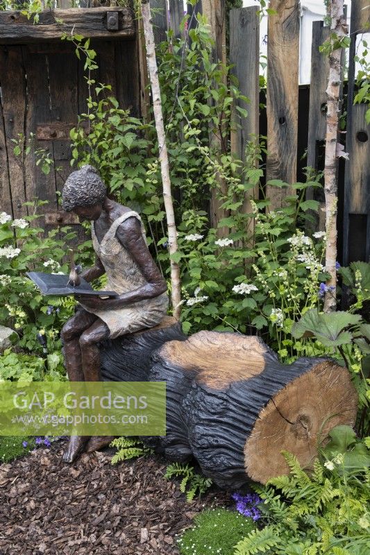 Sculpture en bronze d'une femme intitulée 'Belle' assise sur un rondin de chêne noirci.Dawn Conn Sculpture stand au RHS Chelsea Flower Show 2023