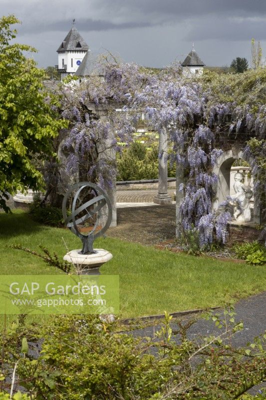 Un cadran solaire armillaire sur socle avec pergola couverte de glycines derrière. Trago Mills montrent les jardins, Devon, Royaume-Uni. Peut. Printemps