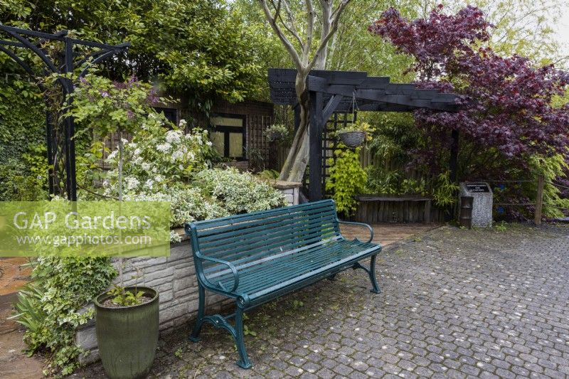 L'un des jardins du spectacle de Canal Street avec un banc en métal et un dallage à l'avant et une pergola en bois à l'entrée du jardin. Trago Mills montrent les jardins, Devon, Royaume-Uni. Peut. Printemps