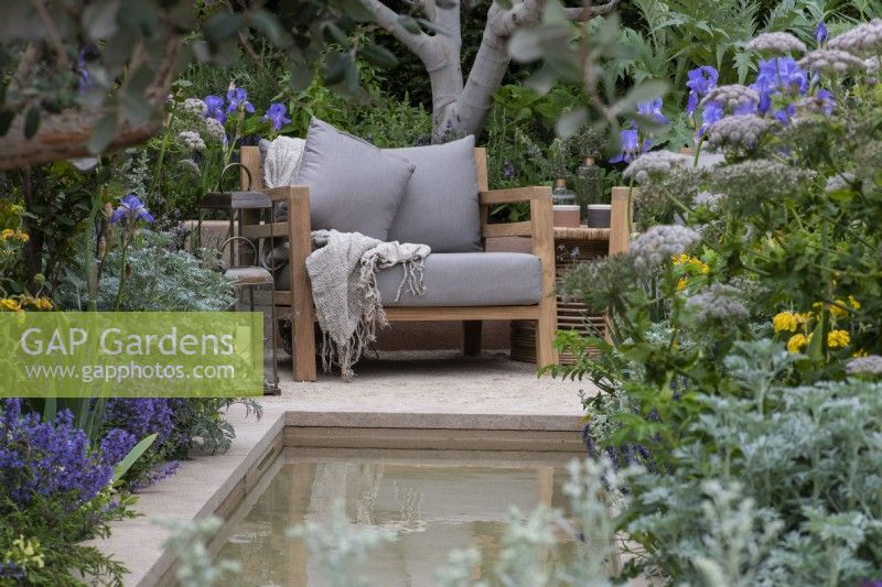 Une chaise surplombe un ruisseau bordé d'armoises à feuilles grises, d'iris, d'ombellifères et d'herbes.