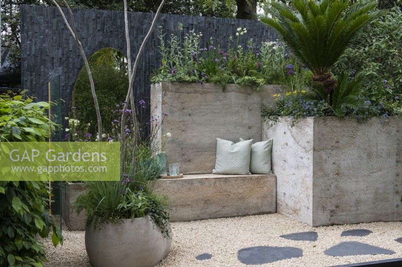 Un jardin de patio urbain avec des sièges et des pots créés à partir d'hypertufa léger et planté de plantes résistantes à la sécheresse. Un miroir reflète la plantation, donnant une illusion d'espace supplémentaire.