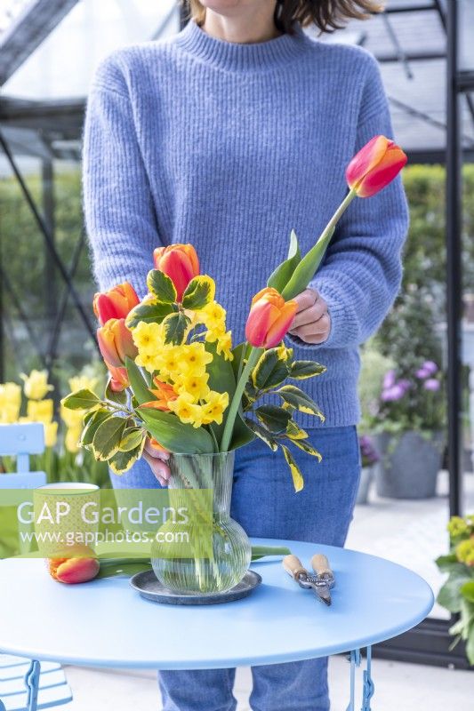 Femme réunissant un bouquet de tulipes et de narcisses à l'extérieur de serre
