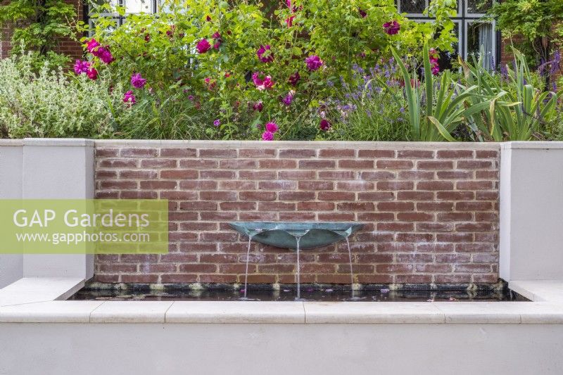 Fontaine bassin vert-de-gris sur mur de briques d'eau en rendu surélevé avec terrasse fleurie avec roses au-dessus.