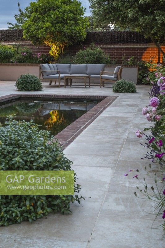 Eclairage de jardin sur terrasse en grès avec bassin rectangulaire et mobilier ; et boules topiaires Pittosporum pour éclairage dissimulé (non visible)