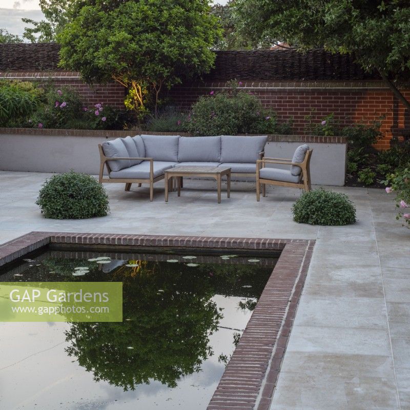 Reflet d'arbre illuminé au crépuscule dans une piscine rectangulaire sur terrasse avec mobilier de jardin