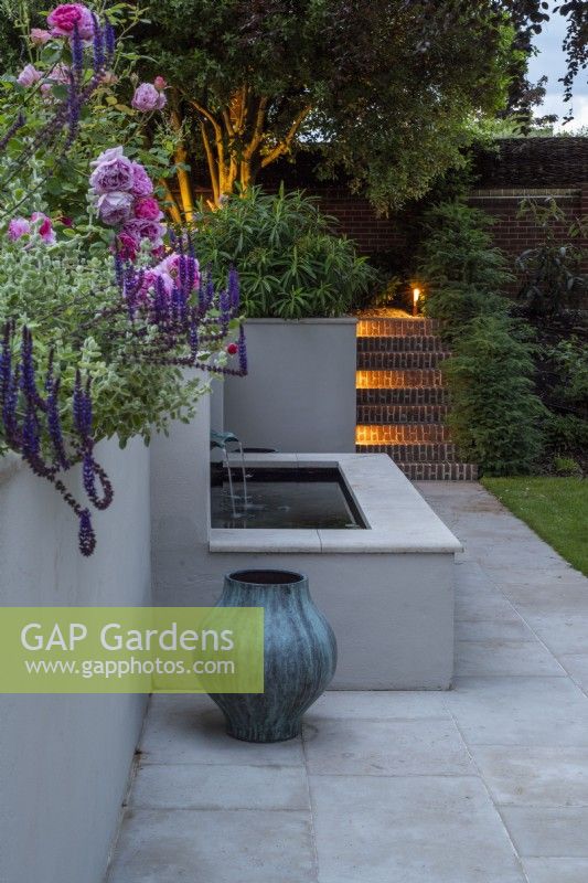 Dispositif d'eau rendu blanc au crépuscule avec pot vert-de-gris avec éclairage de jardin pour les marches en brique en arrière-plan
