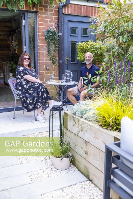 Les propriétaires de jardin assis à table derrière un parterre de fleurs surélevé dans leur jardin