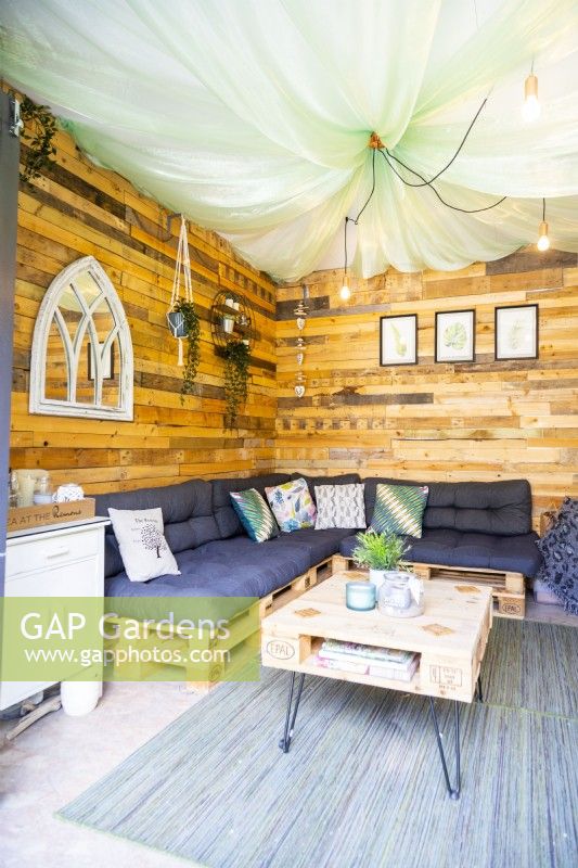 À l'intérieur d'une petite maison d'été avec des murs en bois, des canapés en palettes et une table basse en palettes sur un tapis