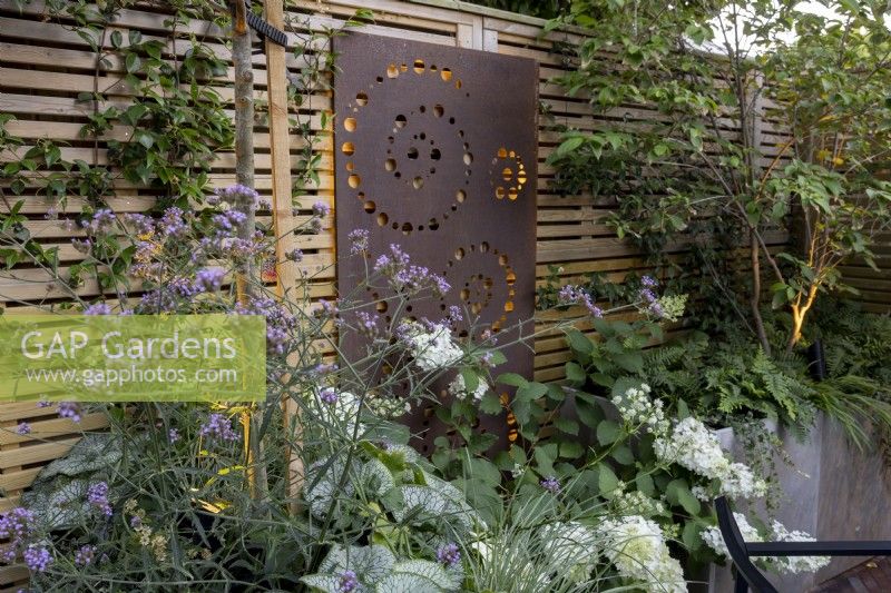 Jardin de cour au crépuscule avec parterres de fleurs surélevés et clôture en bois contemporaine avec écran et éclairage métalliques