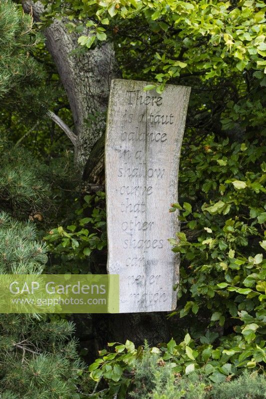 Inscription sculptée sur une planche de bois suspendue à un arbre dans la déambulation. Août.