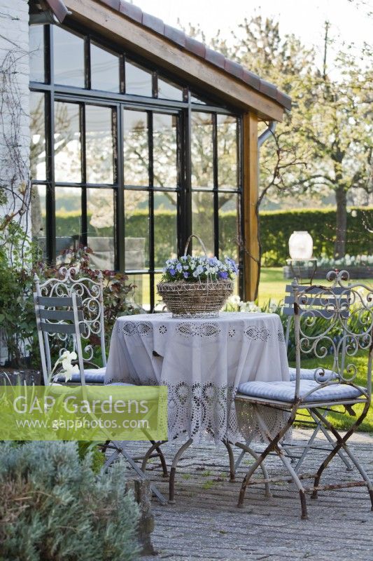 Salon de jardin en métal blanc décoré d'une nappe et d'un panier en métal planté d'Altos.