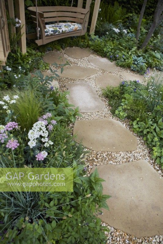 Le jardin communautaire de London Square. Conception : Jardin du sanctuaire James Smith : RHS Chelsea Flower Show 2023. Allée en pierre naturelle et gravier à travers des parterres de fleurs jusqu'au coin salon. Été.