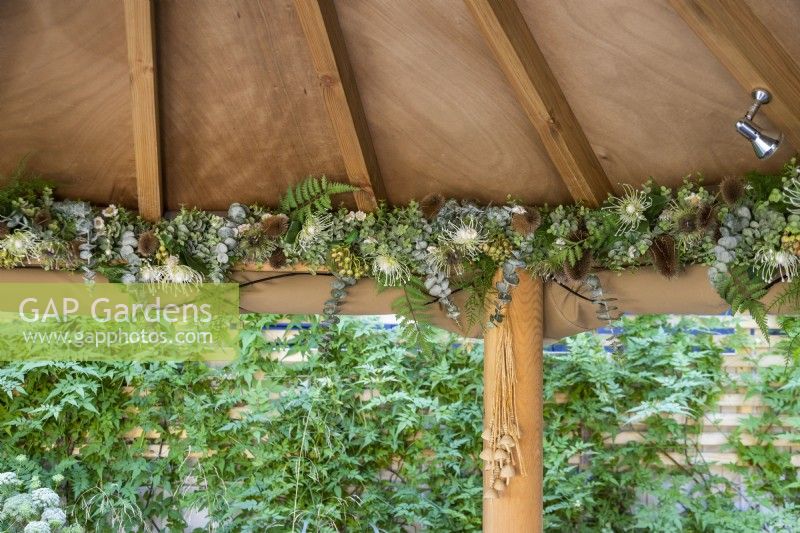 Plantes artificielles et gousses séchées décorant le bord intérieur du gazebo en bois