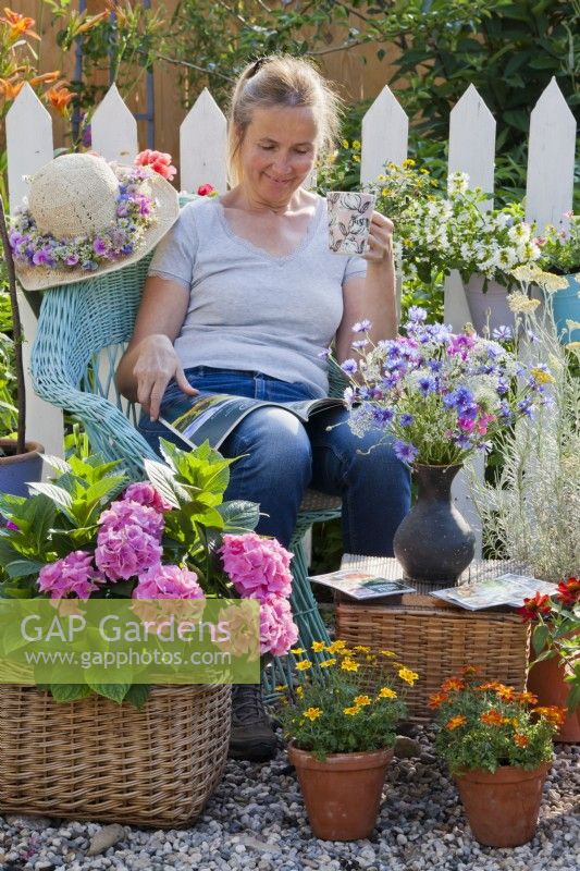 Femme se détendant sur une terrasse en gravier avec des hortensias et des zinnia cultivés en pot.