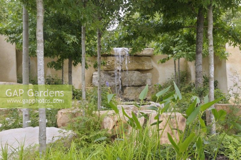 Les plantes et les arbres forestiers encadrent une cascade tombant en cascade sur des dalles rocheuses, offrant un point focal dynamique. America's Wild, présenté par Trailfinders et Visit The USA, RHS Hampton Court Palace Garden Festival 2023.