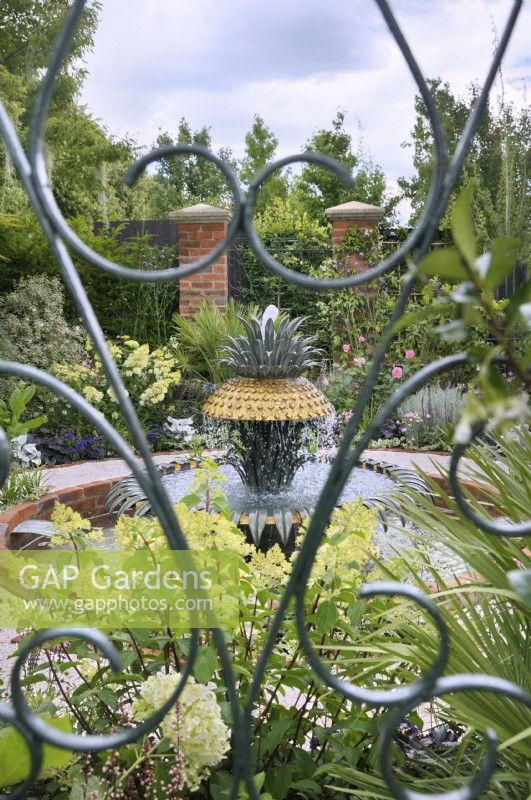 Vue à travers une porte verte en fer forgé d'un jardin formel basé sur les jardins historiques de Charleston, en Caroline du Sud, avec un plan d'eau d'ananas représentant la célèbre fontaine du front de mer de Charleston. Explorez Charleston - Bienvenue à Charleston, RHS Hampton Court Palace Garden Festival 2023.
