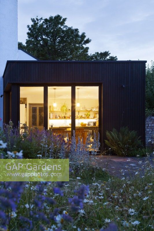 Vue sur les parterres de fleurs et la pelouse de la maison et l'extension de la cuisine moderne au crépuscule.