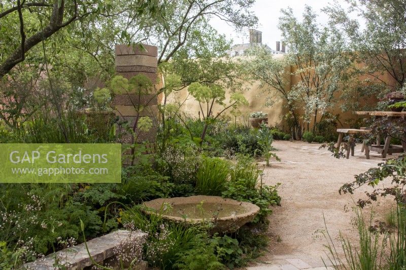 Vue à travers le jardin Nurture Landscapes avec une pièce d'eau circulaire, un mur et une colonne fabriqués à partir de déchets - designer Sarah Price - RHS Chelsea Flower Show 2023