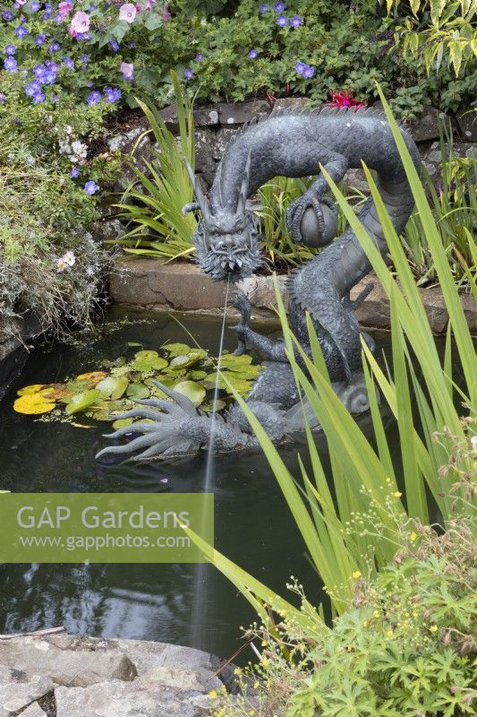 Une grande sculpture de dragon en cuivre, de style chinois, dans un décor d'étang avec un jet d'eau jaillissant de la bouche. Été.