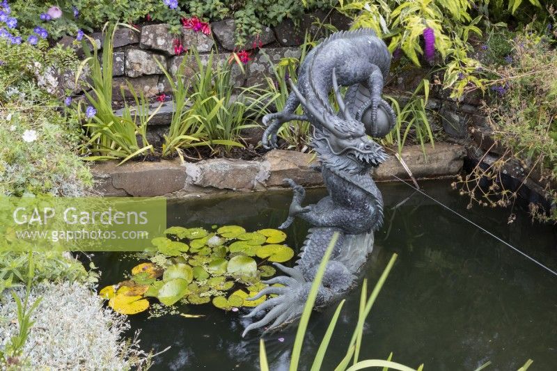Une grande sculpture de dragon en cuivre, de style chinois, dans un décor d'étang avec un jet d'eau jaillissant de la bouche. Été