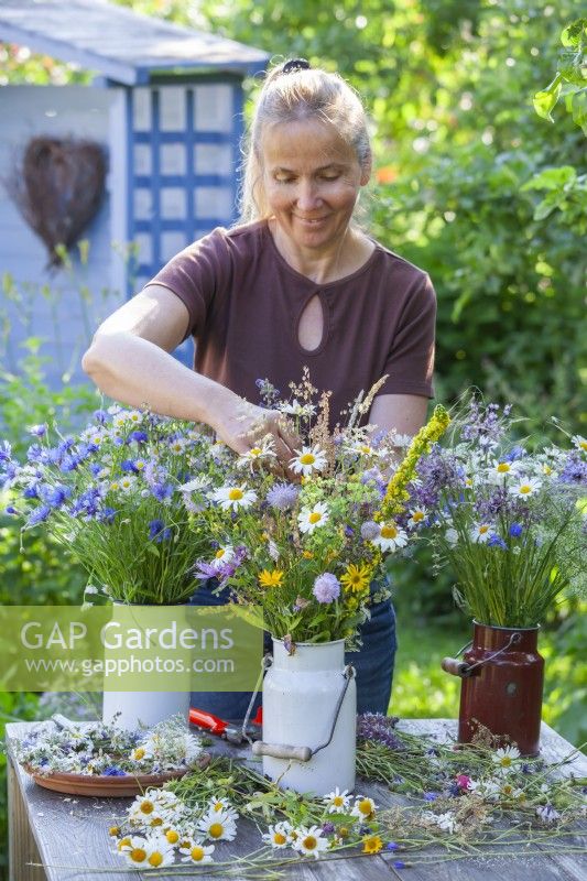Femme faisant des compositions florales à l'aide de marguerites, de bleuets et d'autres fleurs sauvages.