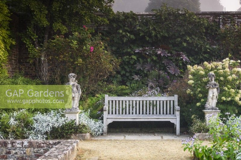 Des chérubins en pierre flanquent un banc en bois dans le jardin clos de Parham House en septembre