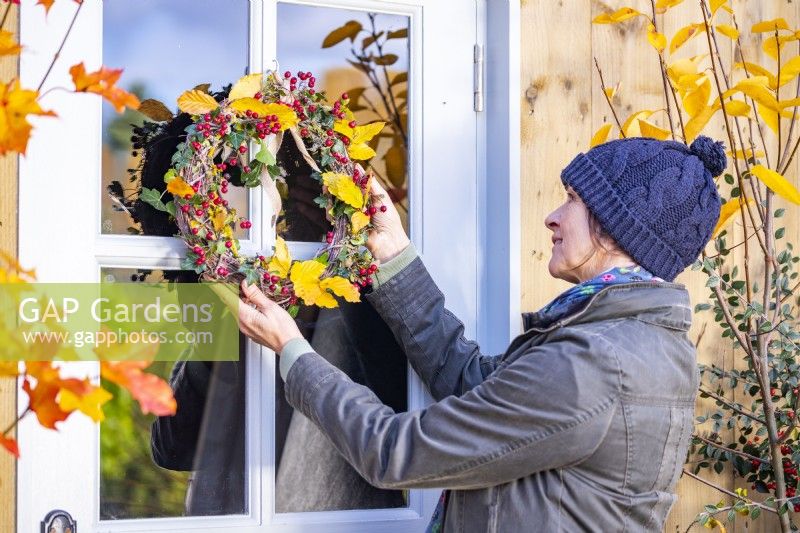 Femme plaçant une couronne faite de lierre, de brins de hêtre et d'aubépine sur une porte