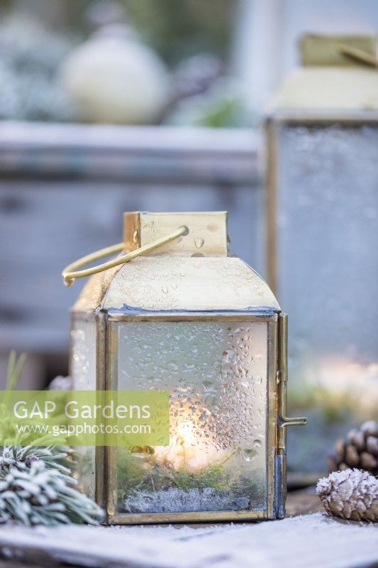 Petites lanternes avec de l'eau sur verre provenant du gel fondu avec des brins de pin et des pommes de pin sur des caisses en bois - couvertes de givre