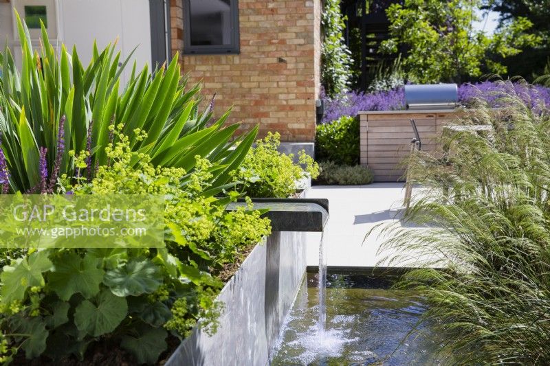 L'eau courante du bec verseur dans un parterre métallique surélevé dans un jardin moderne