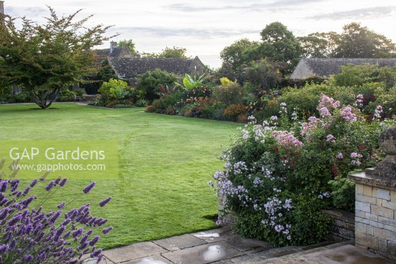 Des marches depuis la promenade surélevée mènent à la pelouse principale avec vue sur le parterre de fleurs Warn à Bourton House, Gloucestershire.