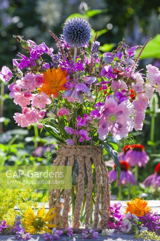 Bouquet d'été avec pois de senteur, roses, monarda, souci, échinops, persicaria et coquelicot dans un vase fait maison en pot de verre et corde en papier.