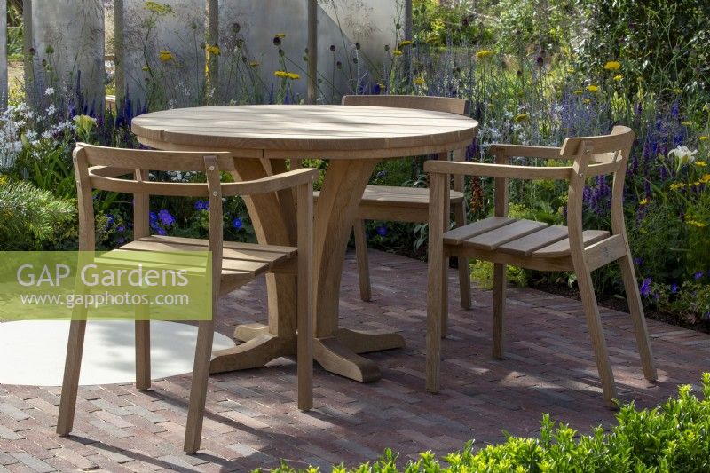 Table et chaises en bois sur un patio pavé de briques - écran métallique en acier, plantation de plantes vivaces mixtes 